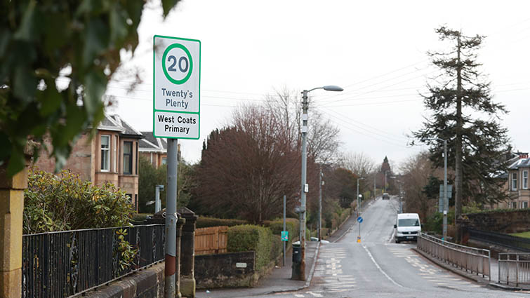 this is a picture of a residential street with trees growing on either side. to the upper left a 20mph speed limit sign is visible