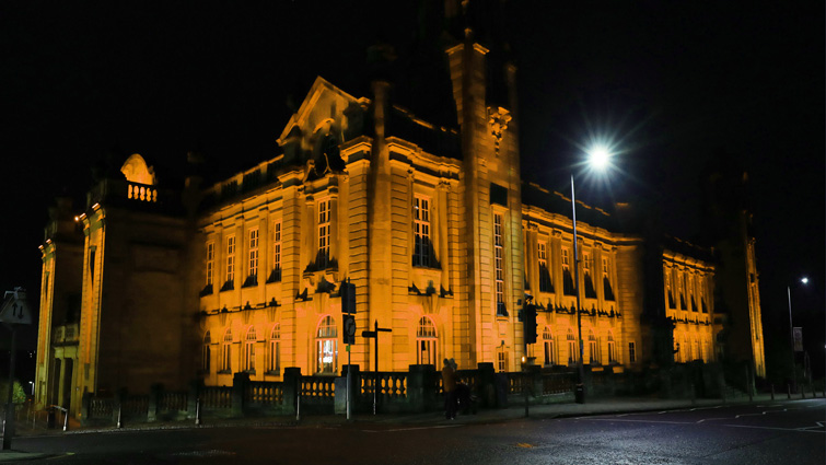 A picture of Hamilton Town House at night with orange floodlighting