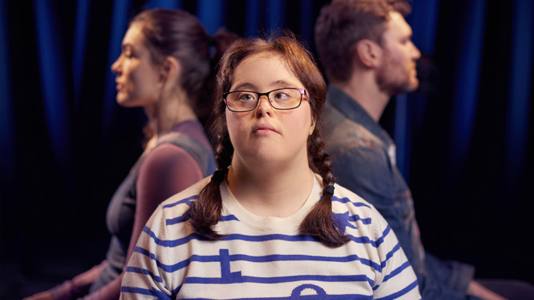This photo is a promotional one for the play showing the main character, Beth facing the camera, with the two other leads, one male, one female, sitting back to back behind her in profile.
