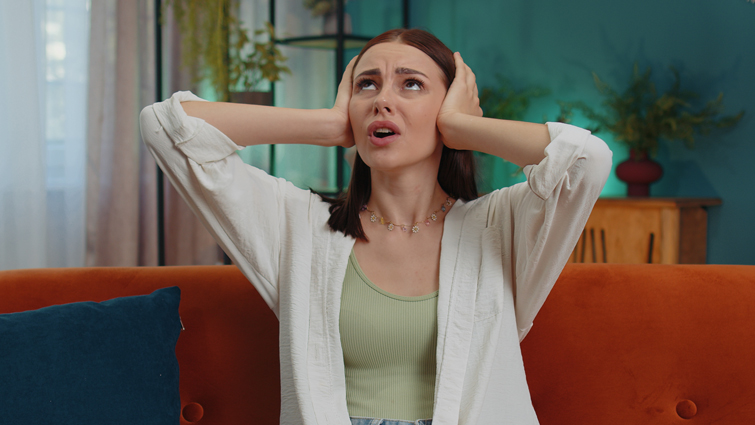 This image shows a woman with her hands over her ears to depict trying to drown out noise