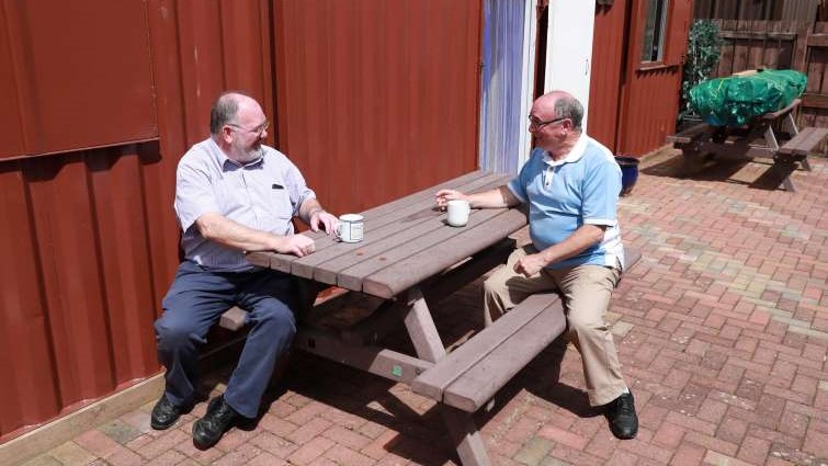 This image shows two men having a chat and cup of coffee outside one of South Lanarkshire's men's sheds