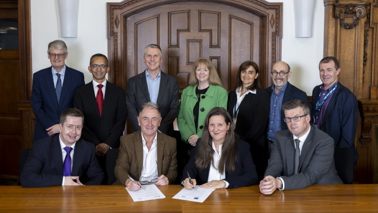 Representatives of all of the partnership organisations are pictured in a line up around a table where the NHSL chief executive and University Professor are signing the agreement.