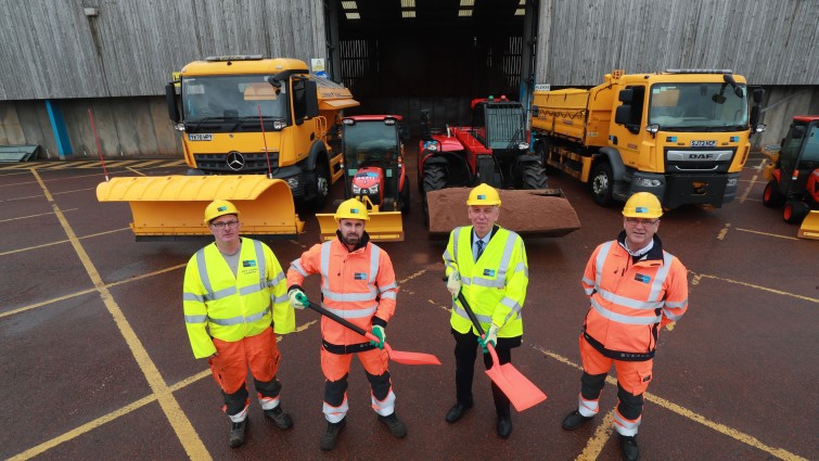 Councillor Robert Brown stands with three of the team from Canderside depot with the salt barn and two winter vehicles behind them.