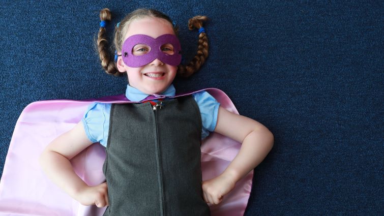 Five-year-old Ellie, wearing her eye mask and cape with hands on hips.