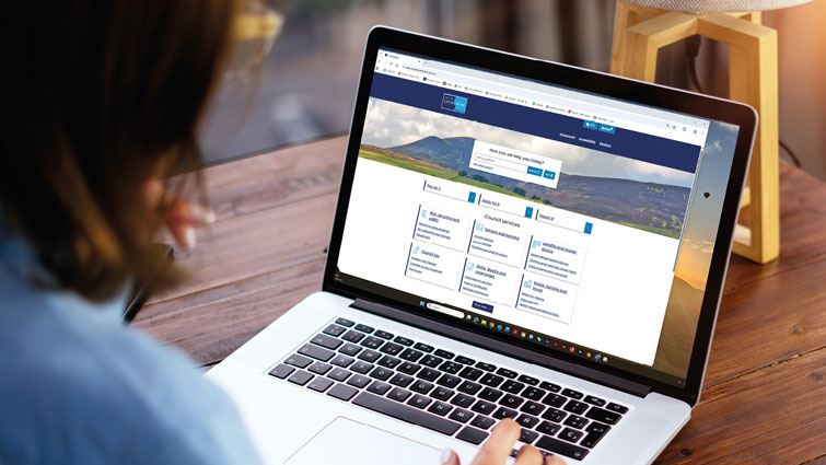This image shows the back of someone looking at a laptop with the home page of the new council website on the screen