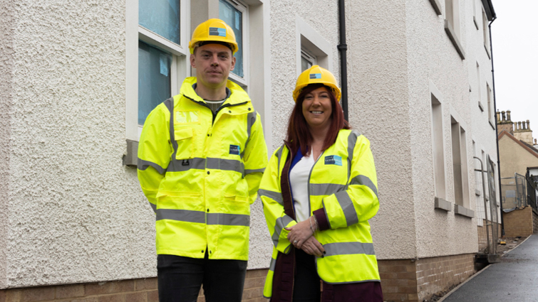 This image shows two council employees in front of new homes being built in Strathaven 