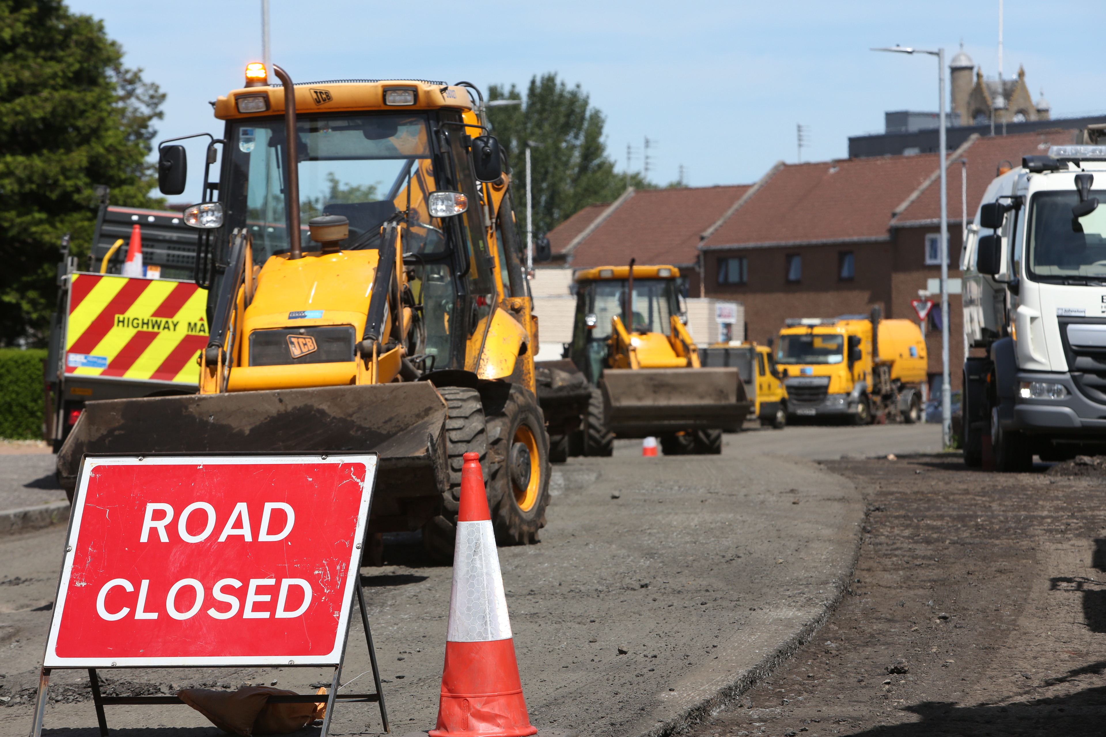 Roadwords with road closed sign and resurfacing equipment and vehicles. 