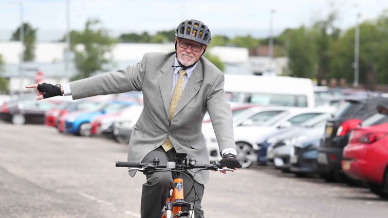 South Lanarkshire Council Leader cycling towards the photographer with his right arm outstretched giving a turn signal. 