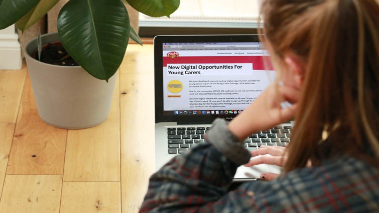 This picture is taken over the shoulder of a young person who is looking at the new opportunities for young carers website on a laptop.