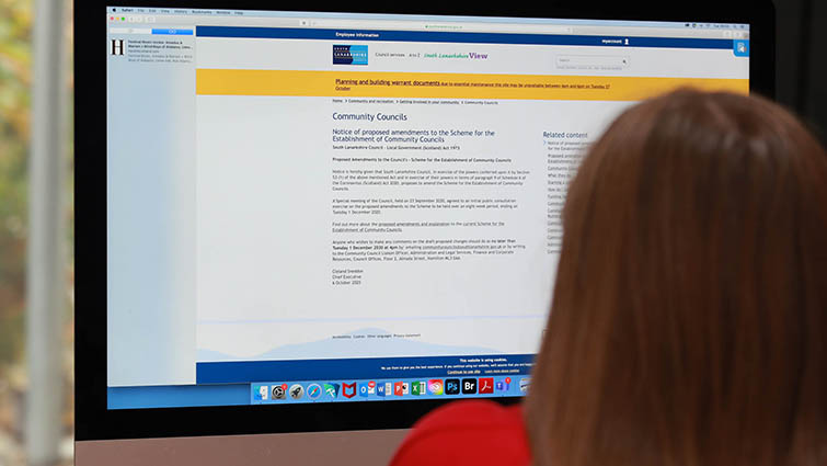 This is a photograph looking over a persons shoulder at a computer screen. On the computer screen is the webpage for the consultation to amend community council meeting regulations.