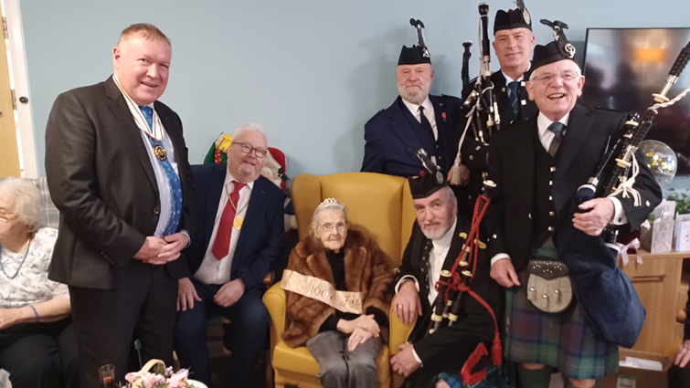 Deputy Lieutenant David Russell and Deputy Provost Bert Thomson wish Margaret McNeil a happy 100th birthday, along with pipers who had played a tribute to her. 