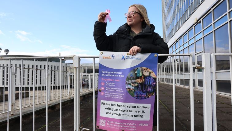 This image shows Councillor Lynsey Hamilton looking at a ribbon which people can attach to the railings outside council HQ during Baby Loss Awareness Week