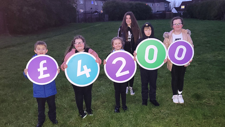 This image shows young people who will benefit from the community garden in Burnhill holding the amount of money the group was awarded in cardboard cut out numbers 