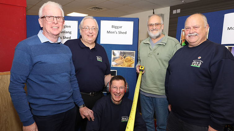 The photo shows four members of the Biggar and District Men's Shed gathered together at an event in 2019. 