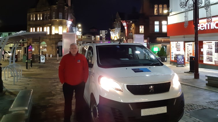This image shows a community warden next to his vehicle with Christmas decorations in the background