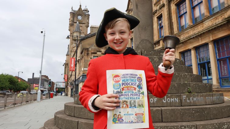 primary school pupil dressed up as a town crier outside Rutherglen Town Hall holding a podcast poster as part of the town&rsquo;s 900th anniversary celebrations
