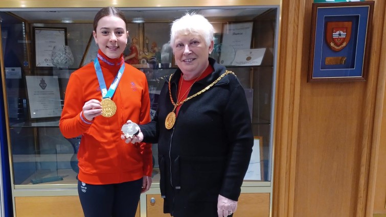 This image shows Holly in Team GB tracksuit and wearng her gold medal, standing with Provost Cooper who is presenting her with a silver trinket box. 