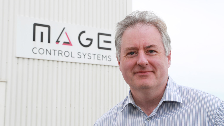 This image shows Mage Control Systems Managing Director Matthew Love in front of a sign for the company 