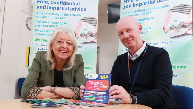 This image shows Councillor Lesley McDonald and a member of the council's Money Matters advice service sitting at a table with leaflets in front of them and Money Matters banners behind them