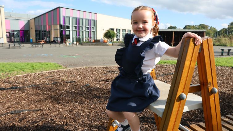 A young pupil standing outside a school.