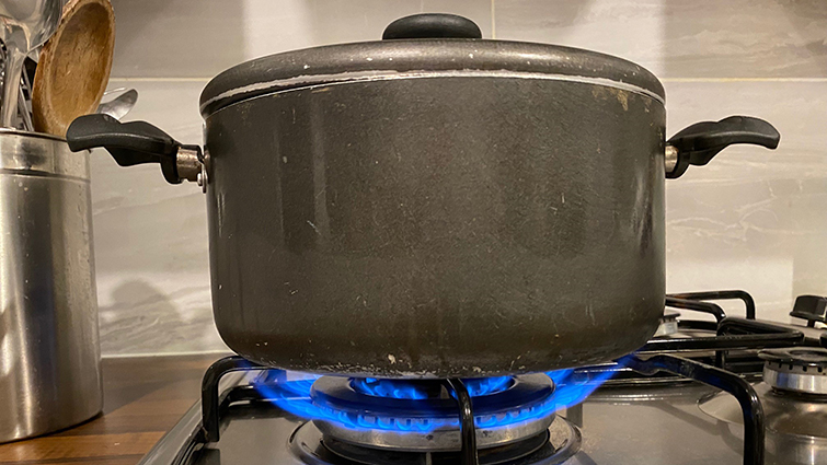 A pan sitting on a gas hob, showing the blue gas flame. 