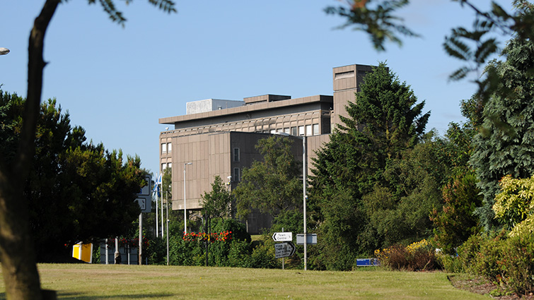 This photograph shows the East Kilbride Civic Centre building, in the foreground there is a grass covered slope and there are tree to either side. 