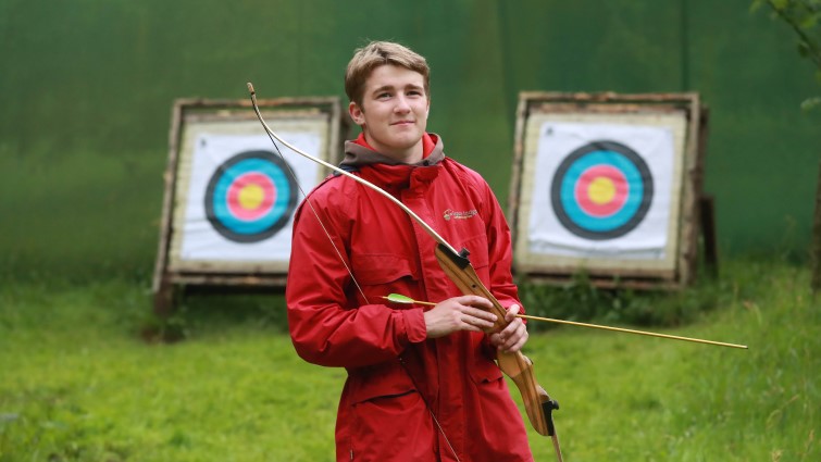 Rowan is pictured on site at wiston lodge holding a bow and arrow, Behind him are two archery targets.