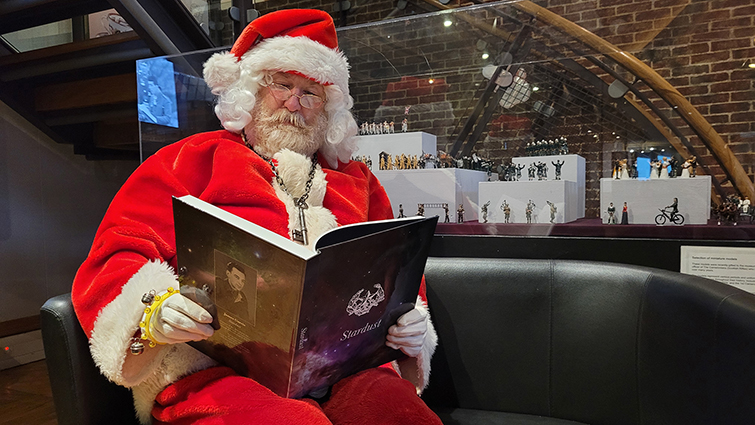 This image shows Santa reading a copy of Stardust, a book about the magazine produced during WWII to entertain Cameronian soldiers