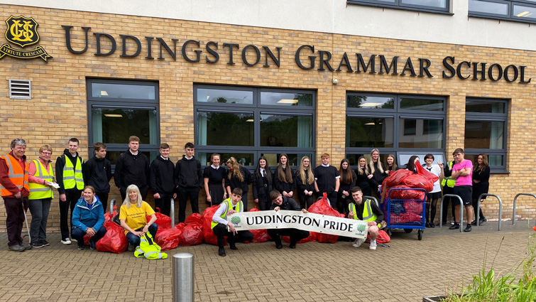 This photo shows a group of around 100 pupils outside Uddingston Grammar school. They are lined up, holding a banner with the Uddingston Pride name on it and are also holding some of the bags of rubbish they collected it.