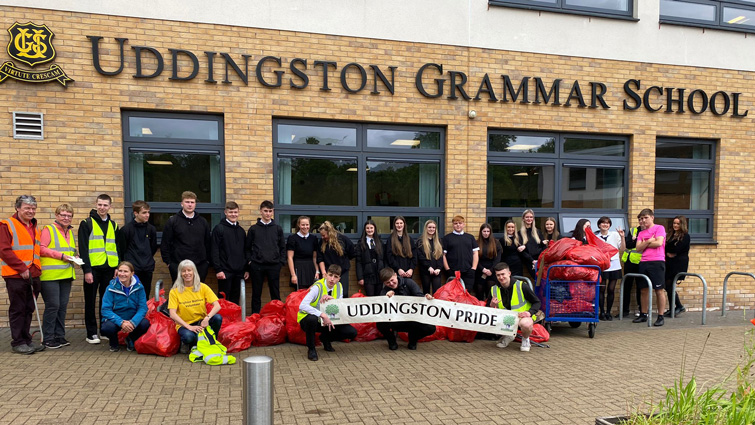 This photo shows a group of around 100 pupils outside Uddingston Grammar school. They are lined up, holding a banner with the Uddingston Pride name on it and are also holding some of the bags of rubbish they collected it. 