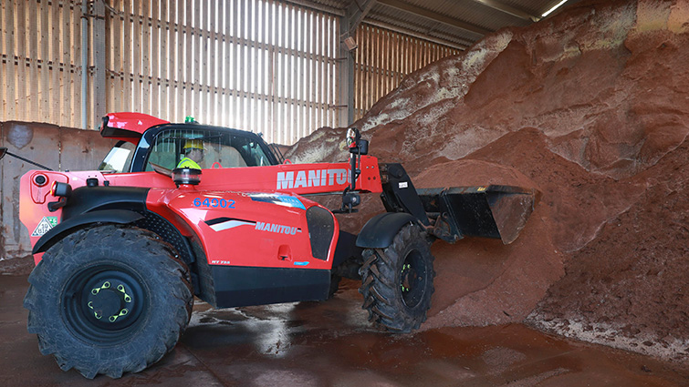 A tractor scooping road grit from a huge pile in a storage building. 