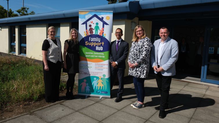 This image shows council leader Joe Fagan, Jenni Minto MSP, Minister for Public Health and Women’s Health, Professor Soumen Sengupta and staff from the Family Support Hub outside it's location in Burnbank, Hamilton with a pop-up banner in between them