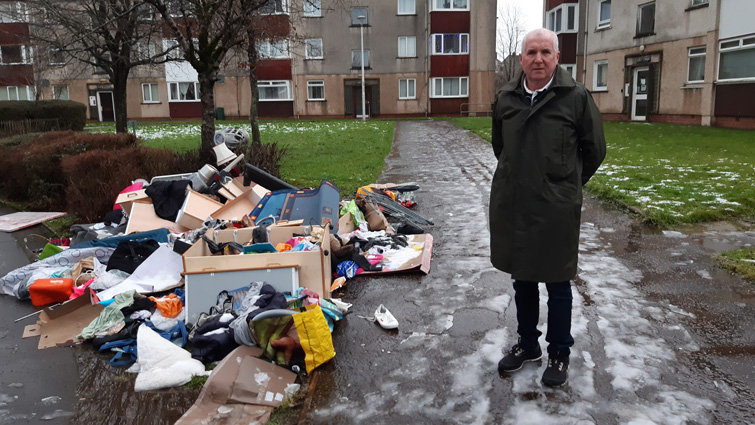 This images shows Councillor John Anderson at a pile of rubbish that has been fly-tipped in East Kilbride 