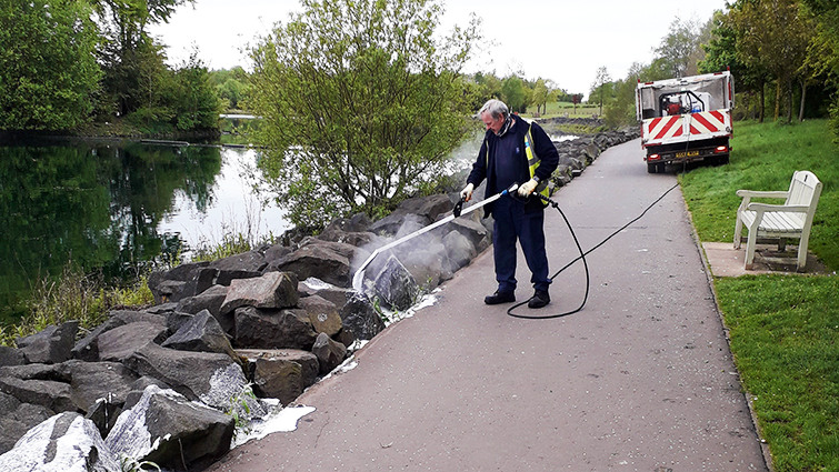This image shows a council employee using hot foam as an alternative to herbicides at a council park 