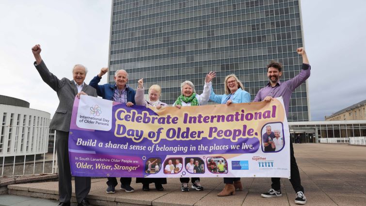 This image shows council staff and members of Seniors Together holding a banner to celebrate International Day of Older Persons outside council HQ in Hamilton