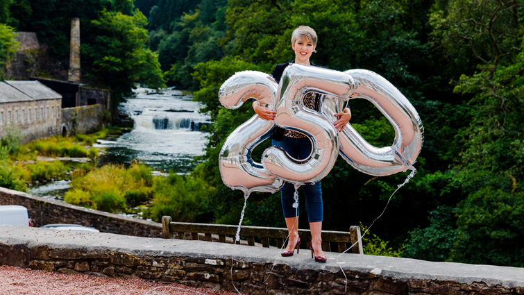 This images shows a member of staff from New Lanark World Heritage site with balloons with the numbers 250 on them to mark the anniversary of the birth of Robert Owen