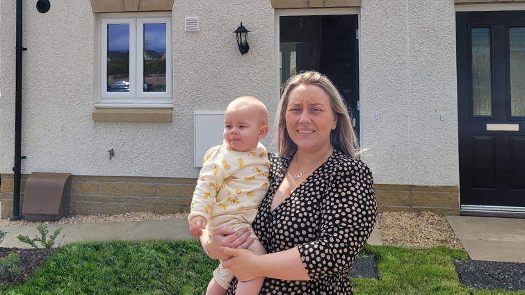 This image shows a new council tenant and her baby outside their property 