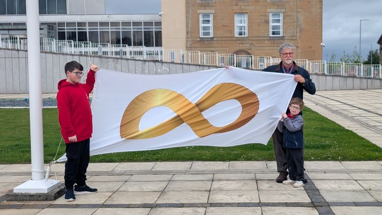 This image shows two young people raising the autism pride flag with ARCH co-ordinator Ramon Hutchingson