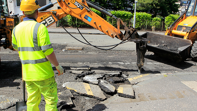 A council worker looks on as a machine breaks up the existing surface to prepare the road for resurfacing 