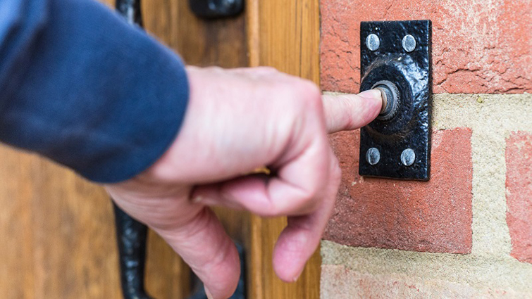 This photo is a close of of a hand ringing a doorbell.