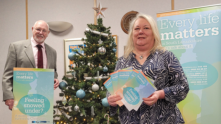 This image shows the council leader and depute leader with a poster and leaflets highlighting the Feeling snowed under – a guide to surviving Christmas campaign 
