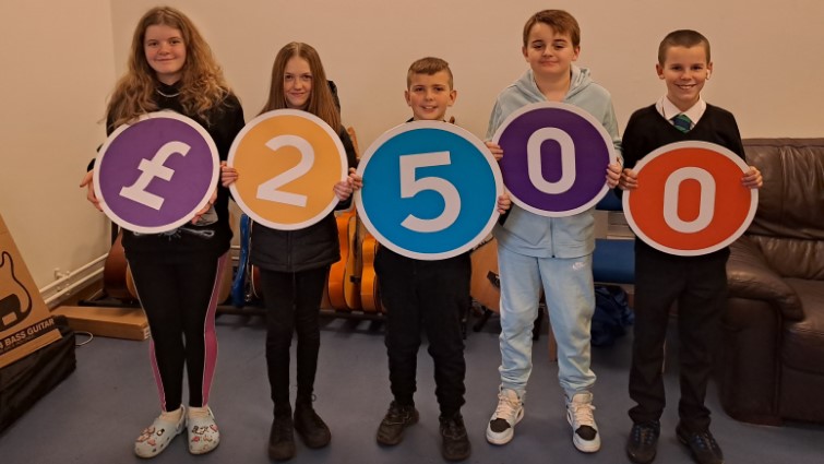 This image shows young people from Whitehill Universal Connections holding up the numbers 2500 which is the amount they were awarded through a Participatory Budgeting exercise 