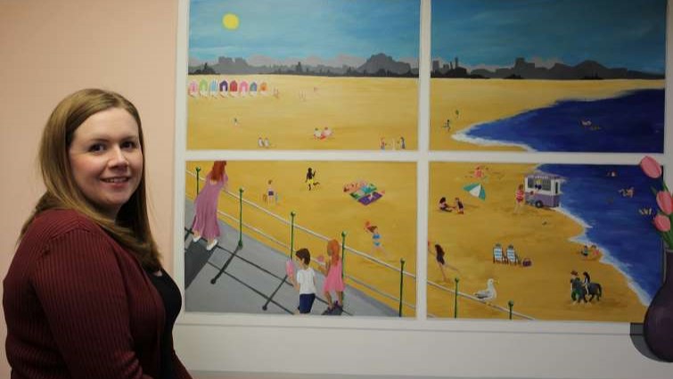 This image shows a member of staff from SLLC at one of the murals done as part of a project at McKillop Gardens care home 