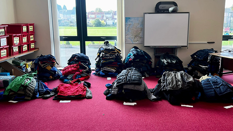 This photo shoes hundreds of donated winter jackets lined up in piles on the floor in a classroom at Townhill primary school. 