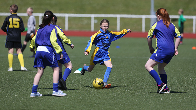 Image shows girls playing football at John Cumming Stadium, Carluke