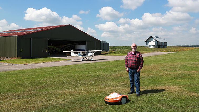 Colin MacKinnon, the Secretary of Strathaven Airfield standing next to a robotic electric mower 