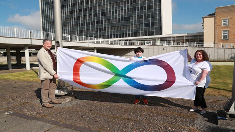 ARCH coordinator Ramon Hutchingson holds the Autism Pride flag with a service user and their child outside the council HQ