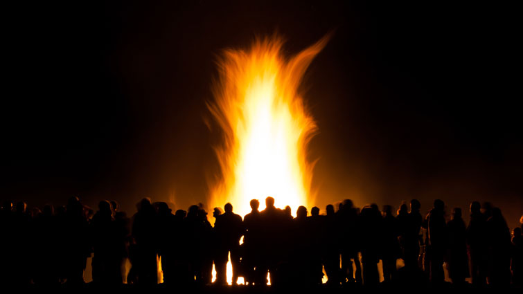 A crowd silhouetted against a large bonfire 