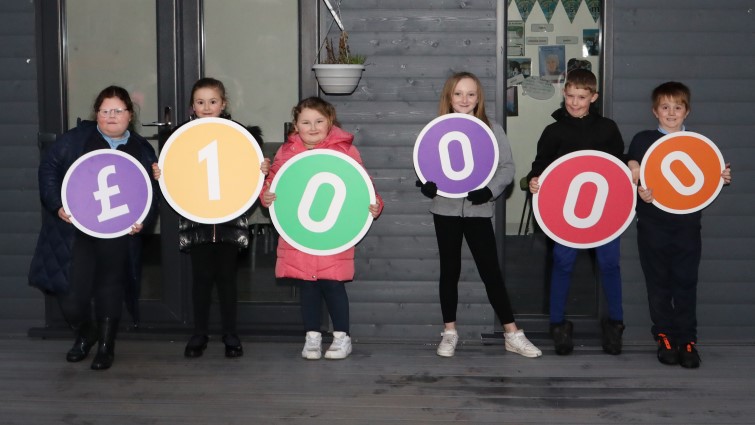 Local children hold coloured signs to show the sum of money, £10,000. 