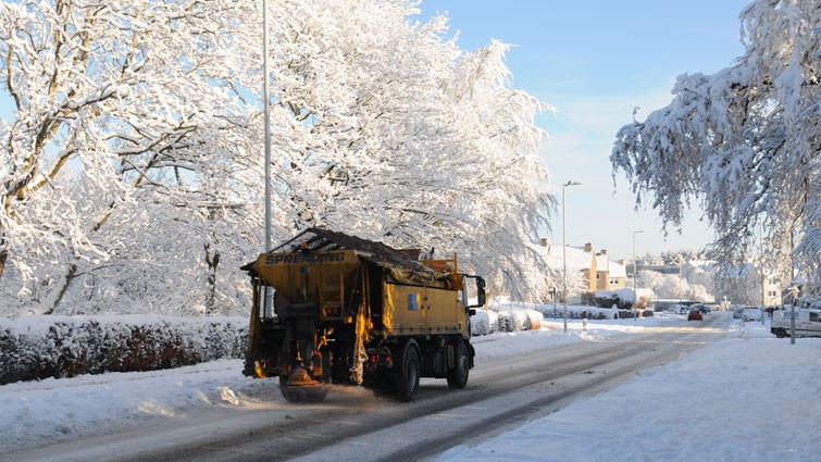 A gritter driving on a snow-covered road in a town.